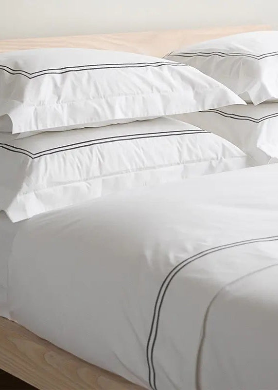 A luxury white bed linen set with a border featuring sateen embroidery, displayed on a bed.