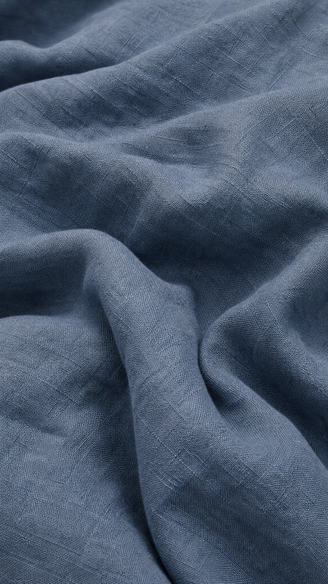 A close-up of draped slate blue linen fabric with a visible woven texture and soft folds.