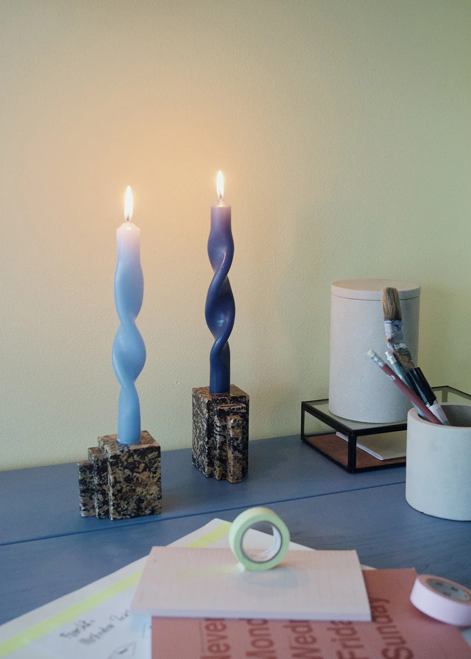Two twisted candles on a desk with office supplies and stationery items.