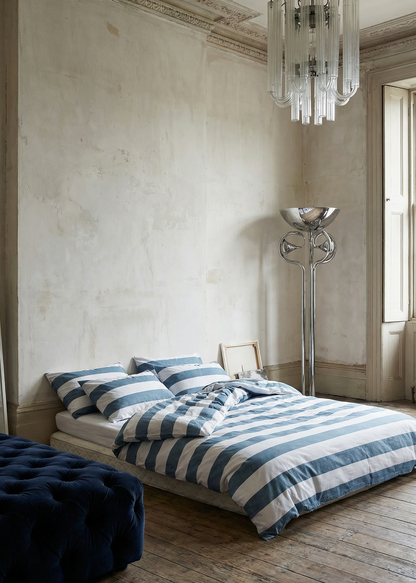 Modern bedroom with striped bedding, chandelier, and floor lamp.