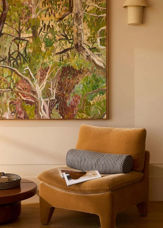 Living room with a mustard chair, round table, and large forest painting on the wall.