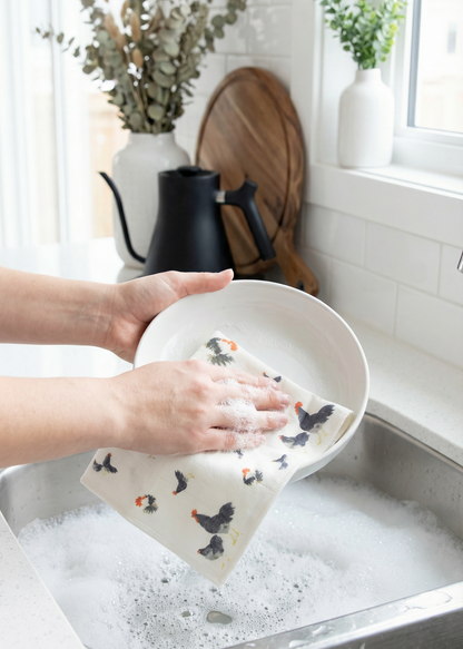 Person washing a plate with a decorative towel in a kitchen sink.