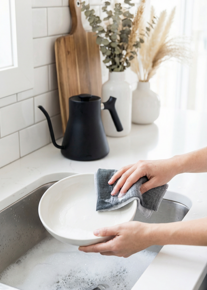 Person washing a white plate in a kitchen sink with a gray dishcloth.