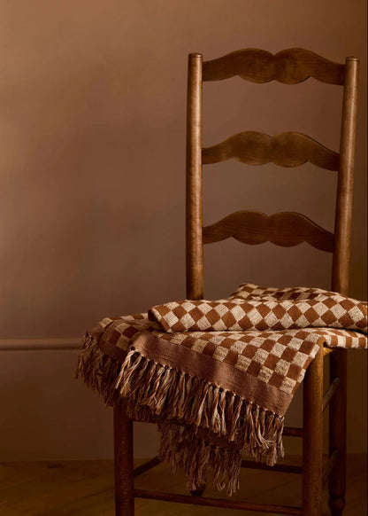 Wooden chair with a checkered blanket draped over it against a brown wall.