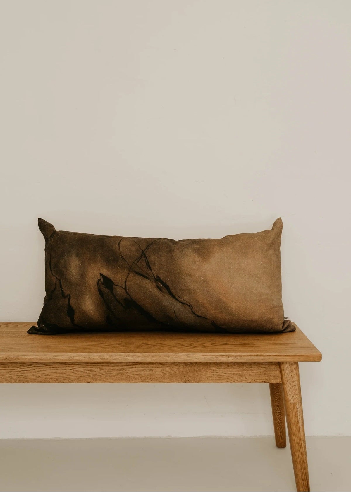 Brown pillow on a wooden bench against a plain wall