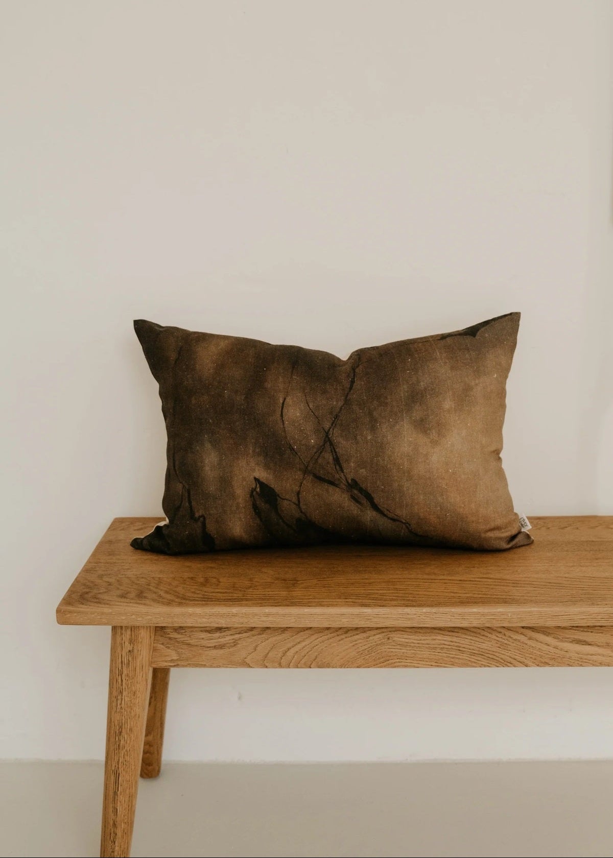 Brown pillow on a wooden bench against a plain wall