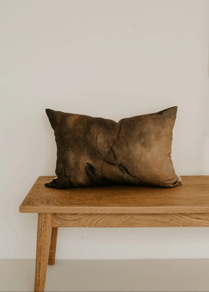 Brown pillow on a wooden bench against a plain wall