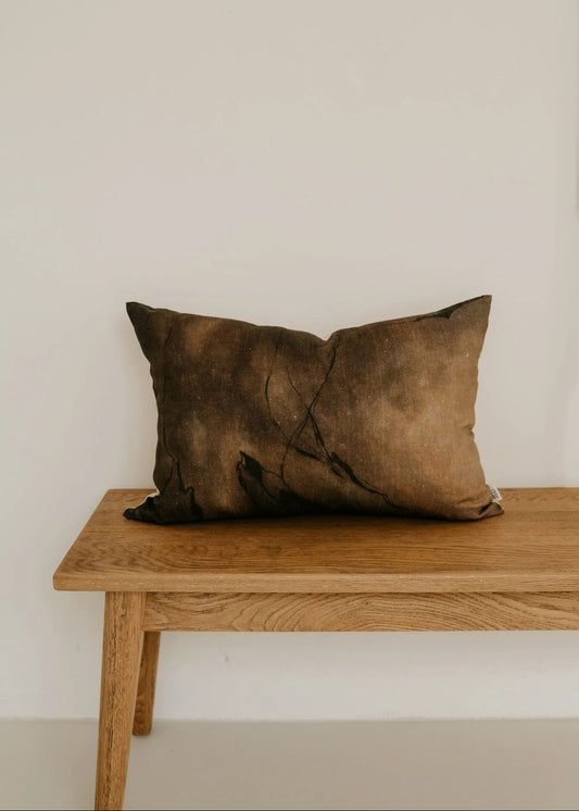 Brown pillow on a wooden bench against a plain wall