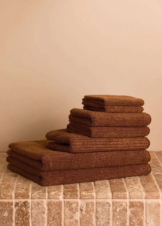 Stack of brown towels on a tiled floor against a beige wall