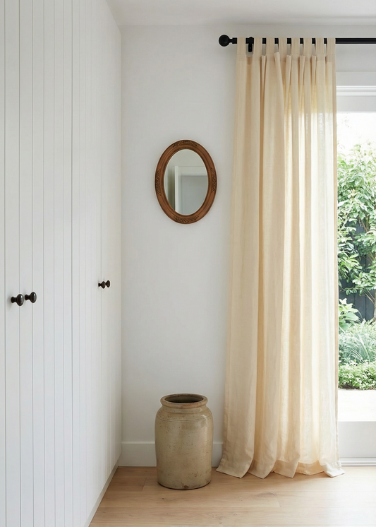 Nest living room with white walls, a large window with beige curtains, a round mirror, and a textured rug.