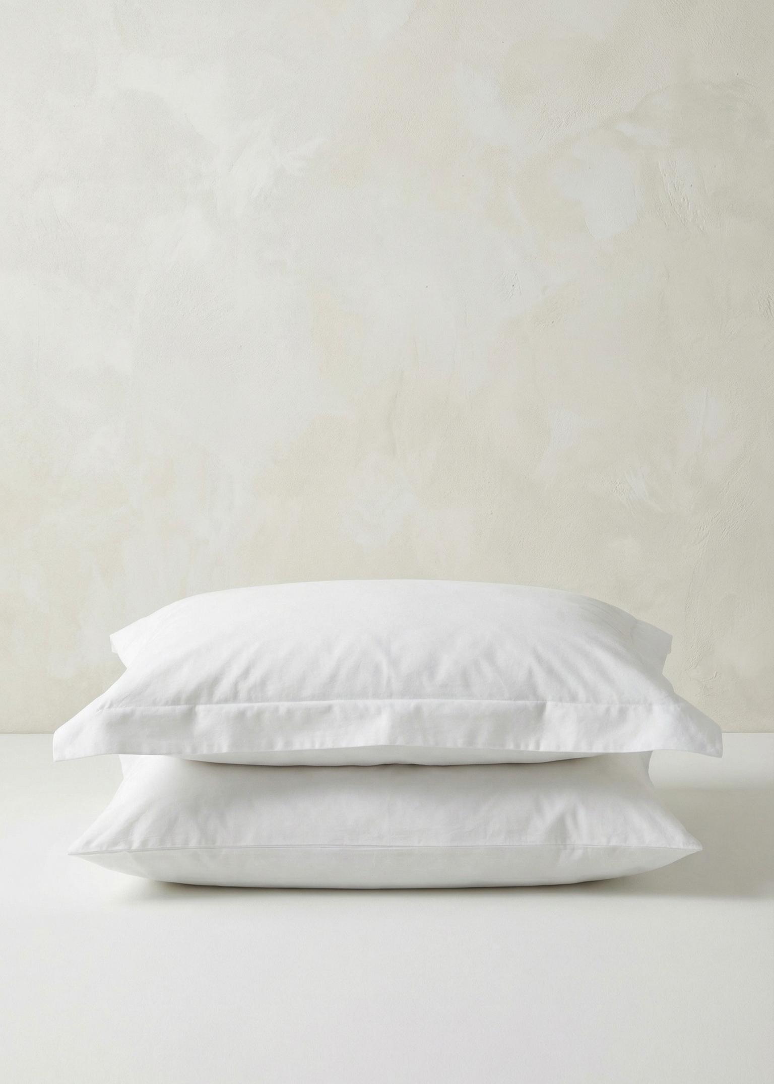 Two white pillows stacked on a light beige background