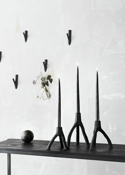 Three black candle holders on a wooden shelf against a white wall with hooks.