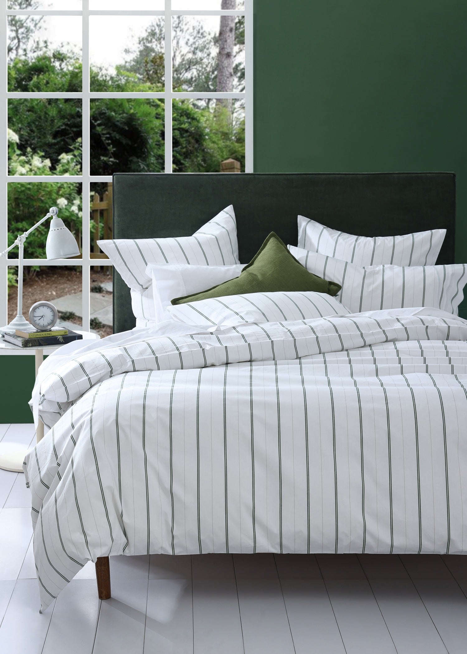 Bed with striped bedding and green pillows in a room with large windows.