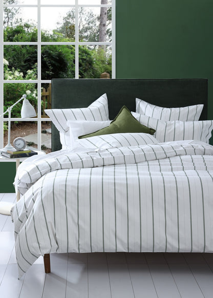 Bed with striped bedding and green pillows in a room with large windows.