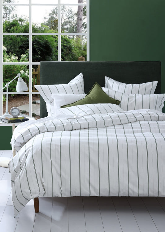 Bed with striped bedding and green pillows in a room with large windows.