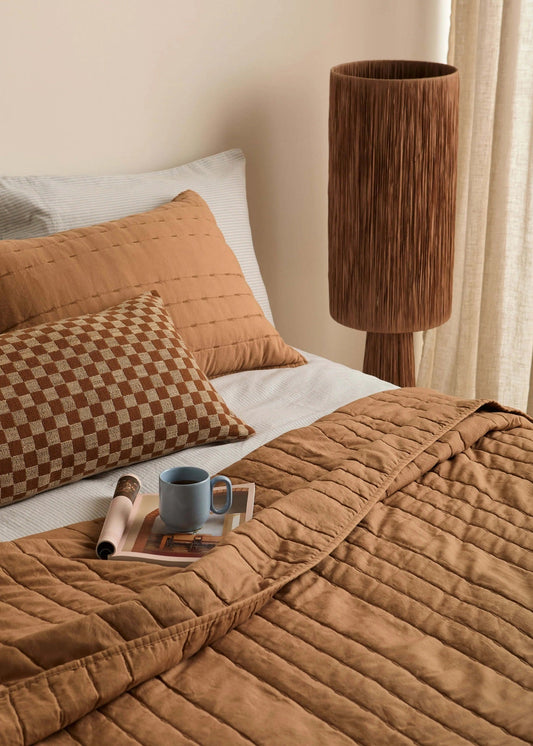 Cozy bedroom with brown quilt, pillows, and a lamp.