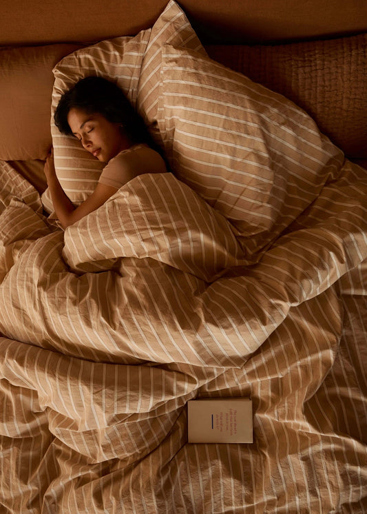 Woman sleeping under striped duvet in a warm-toned bedroom