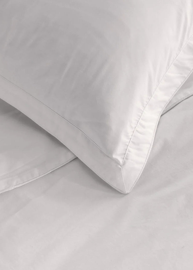 A close-up of a white cotton pillowcase with a piped edge detail.