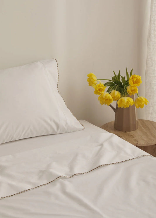 White bed with yellow tulips in a vase on a wooden nightstand.