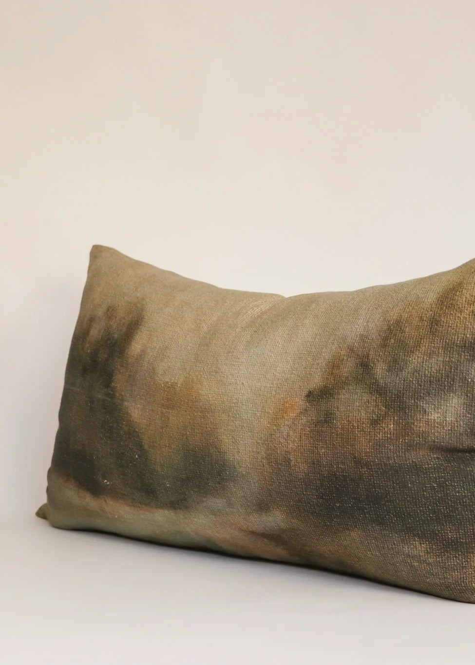 A rectangular lumbar throw pillow with a textured, abstract hand-dyed pattern in earthy tones of brown, olive green, and beige, shown against a plain off-white background.
