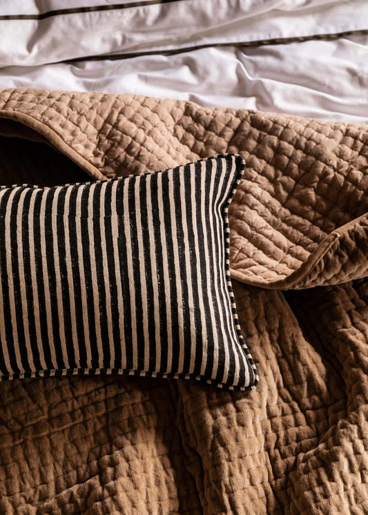 Striped pillow on a textured brown blanket with white bedding in the background