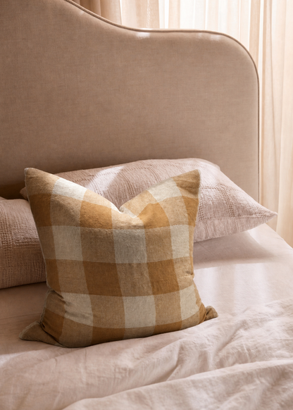 Plaid pillow on a beige sofa with light curtains in the background