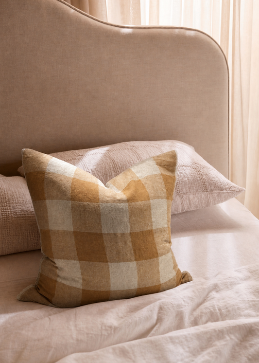 Plaid pillow on a beige sofa with light curtains in the background