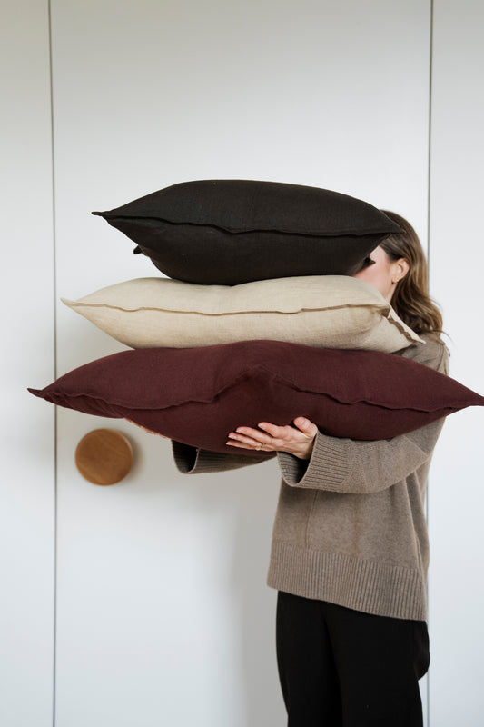 Person holding three pillows of different colors against a white wall