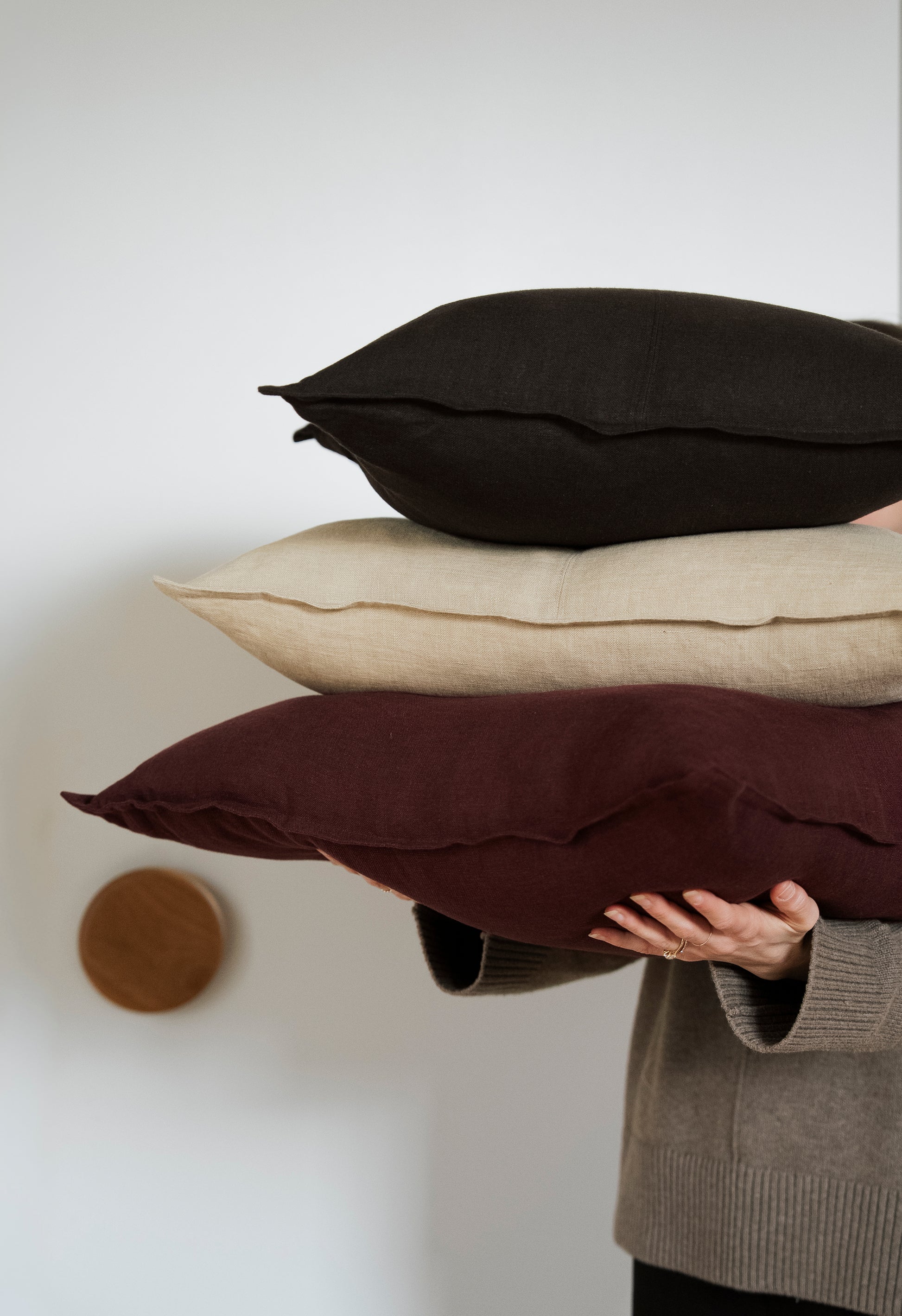 Person holding three pillows of different colors against a plain background