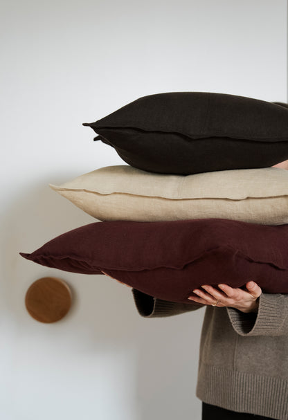 Person holding three pillows of different colors against a plain background