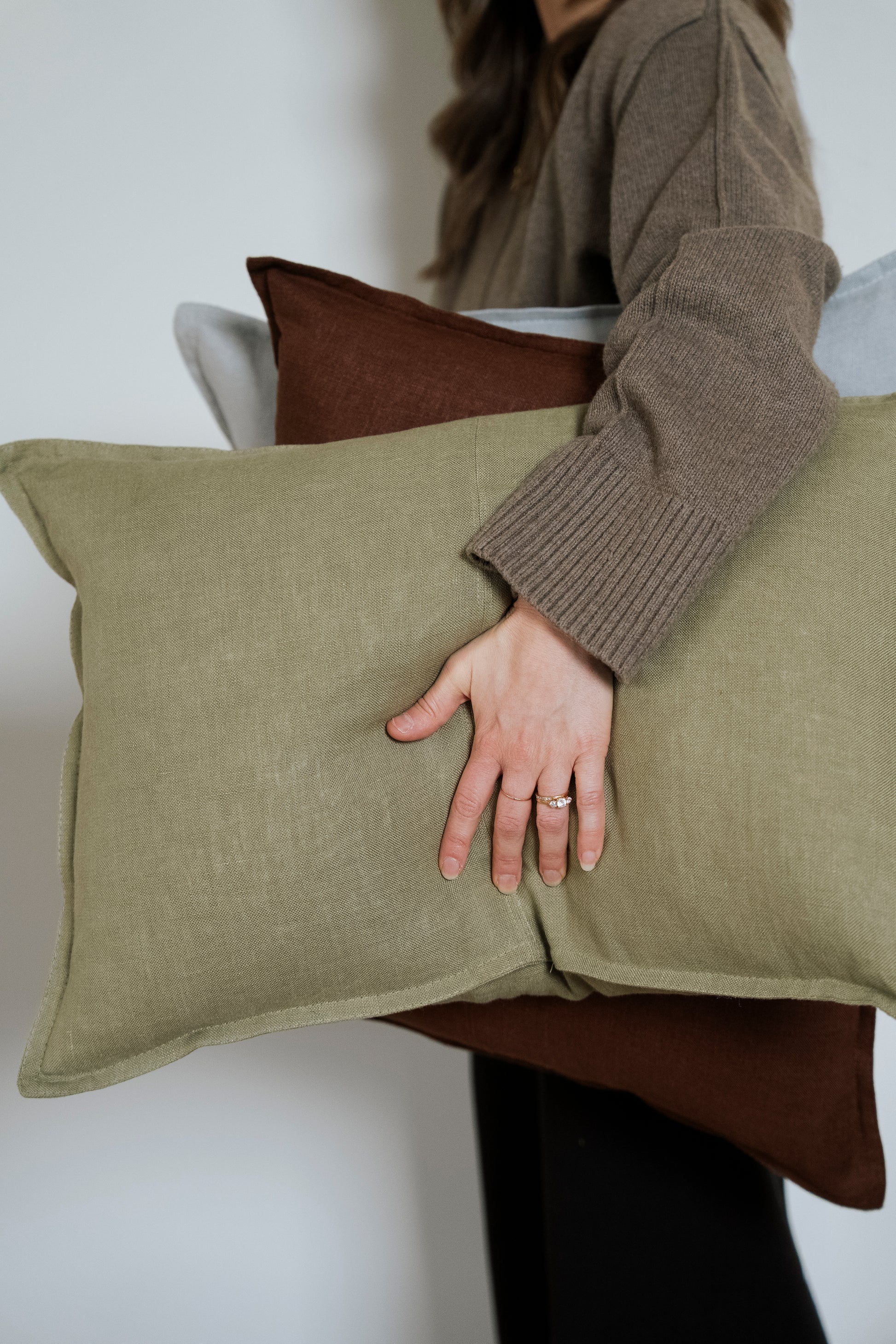 Person holding two pillows, one green and one brown, against a neutral background.