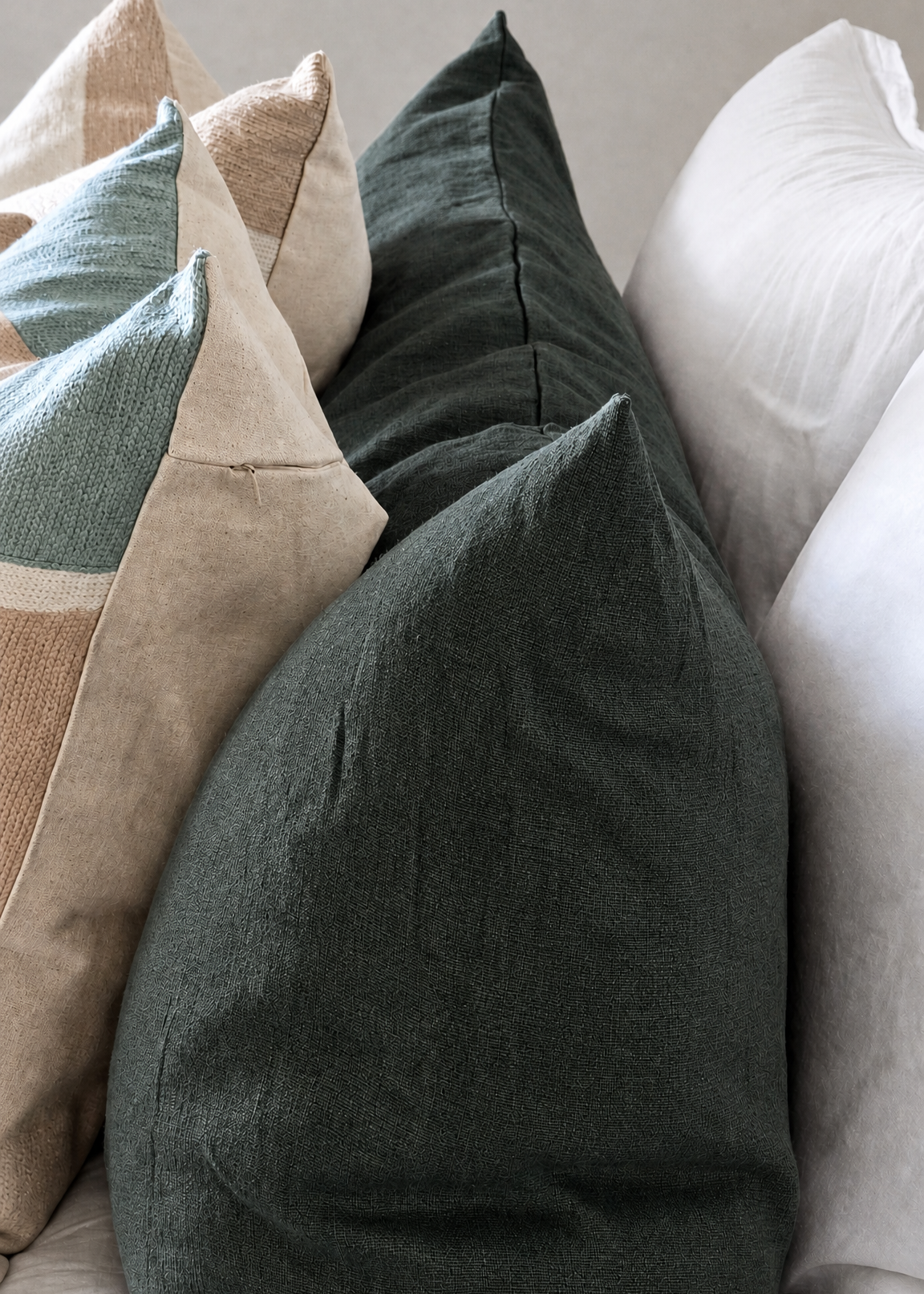 A dark forest green linen throw pillow displayed on a light-colored sofa, surrounded by other neutral-toned pillows.