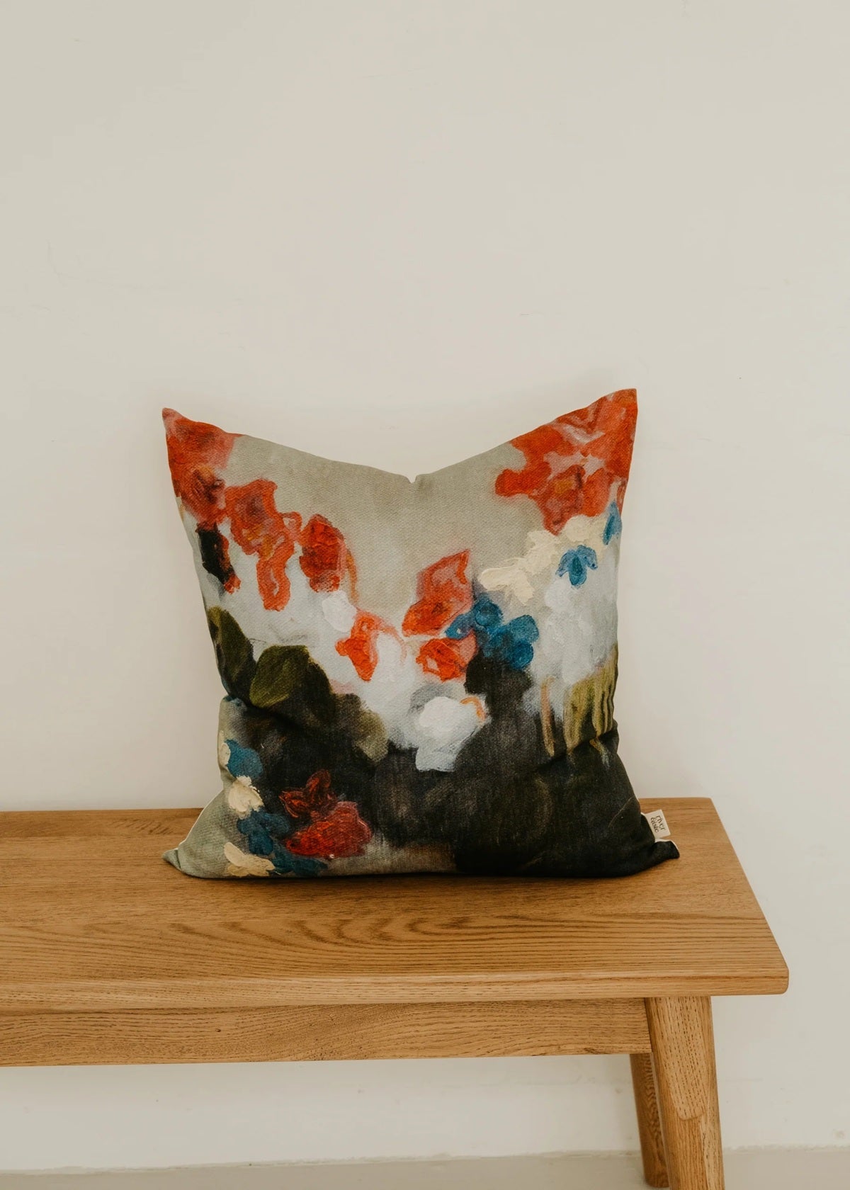 Decorative pillow with colorful floral pattern on a wooden bench against a white wall