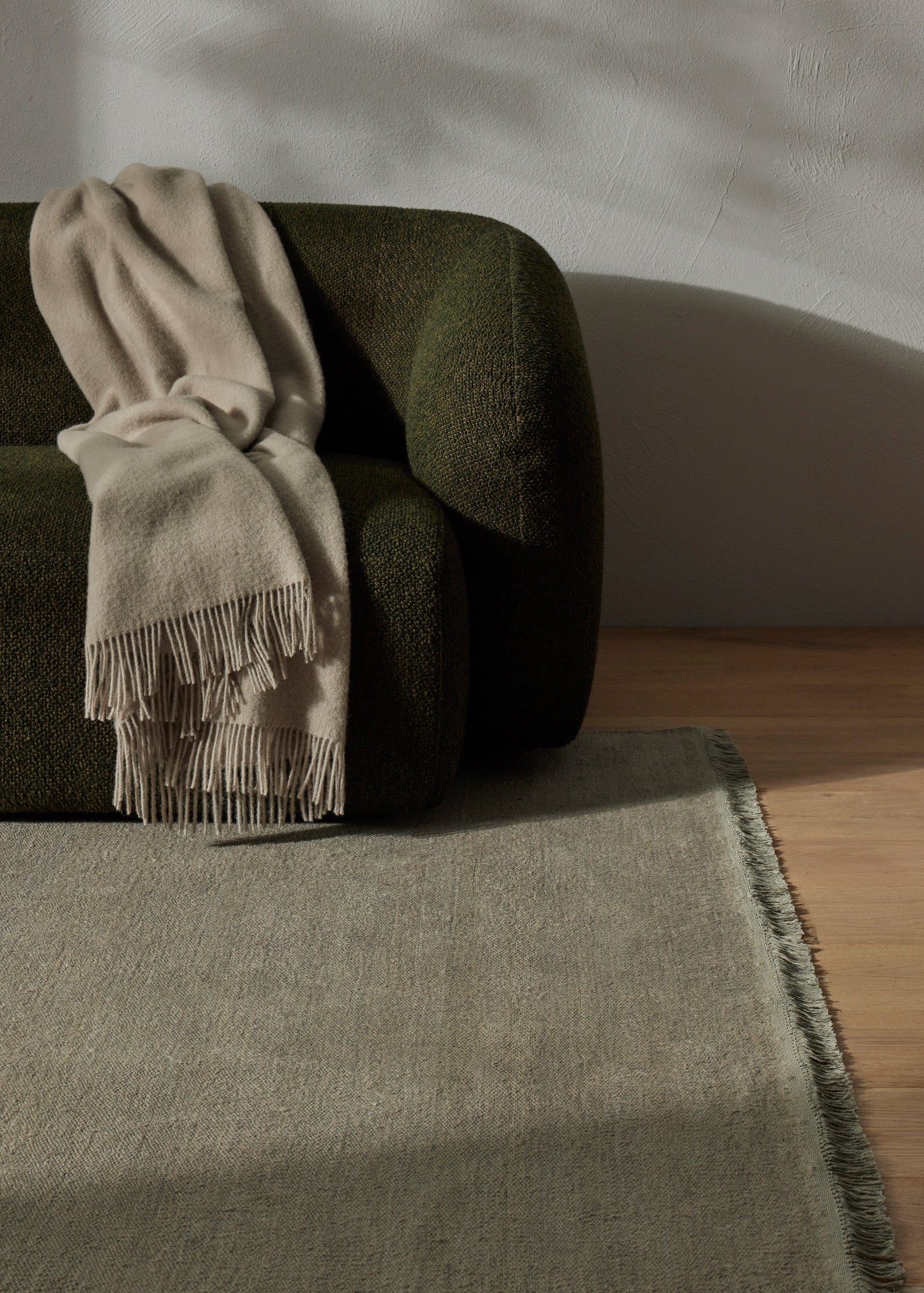 Beige scarf with fringe draped over a green sofa on a wooden floor.