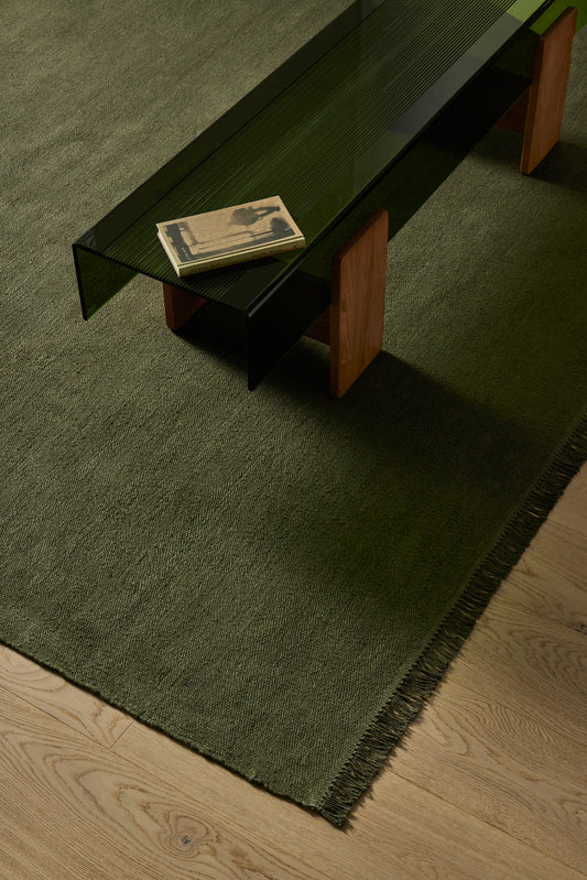 Glass coffee table with wooden legs on a green rug