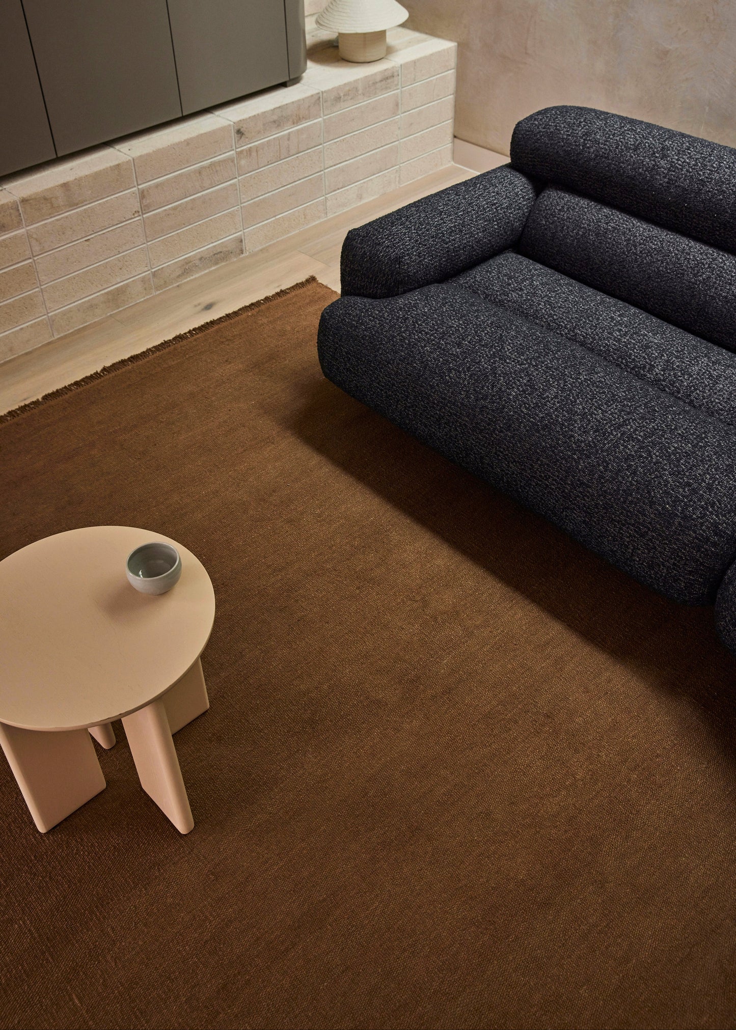 Modern living room with a dark gray sofa, beige side table, and light-colored wall.