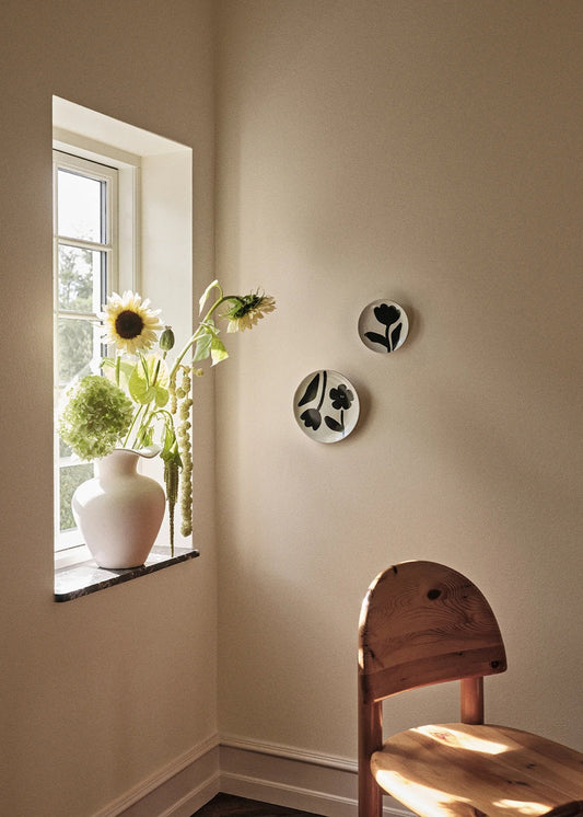 Nestled corner with a vase of flowers by a window, wall decor, and a wooden chair.