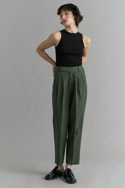 Person wearing a black sleeveless top and green high-waisted pants on a gray background