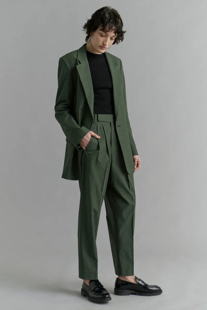 Person wearing a green suit with a black shirt against a gray background