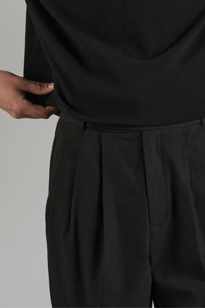 Person wearing a black outfit with pleated pants on a gray background