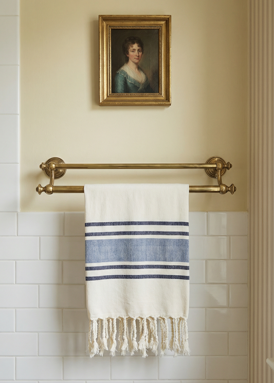 Towel hanging on a brass towel rack with a framed portrait above in a bathroom setting.