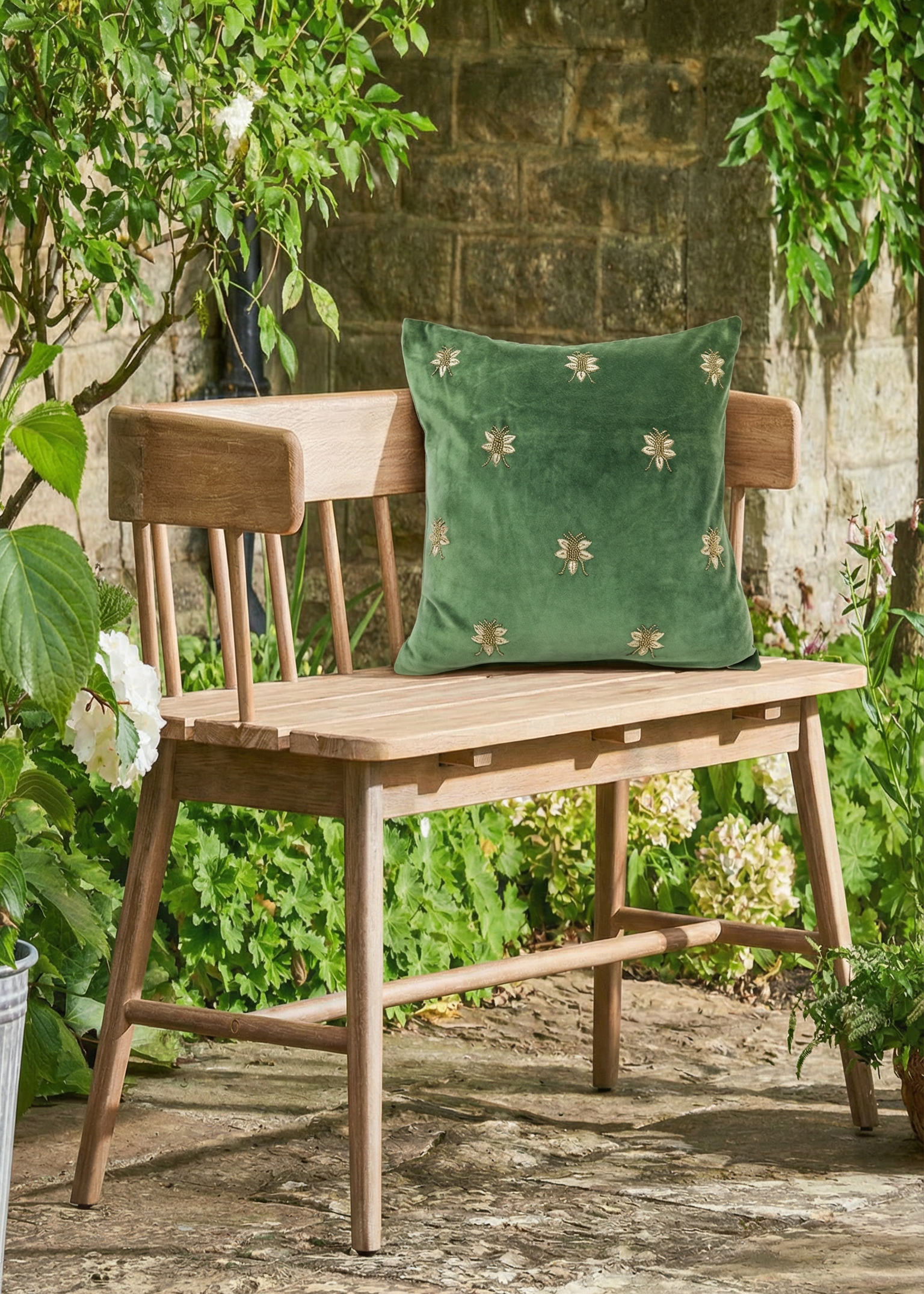 Wooden bench with a green cushion featuring floral patterns, set against a stone wall and greenery.