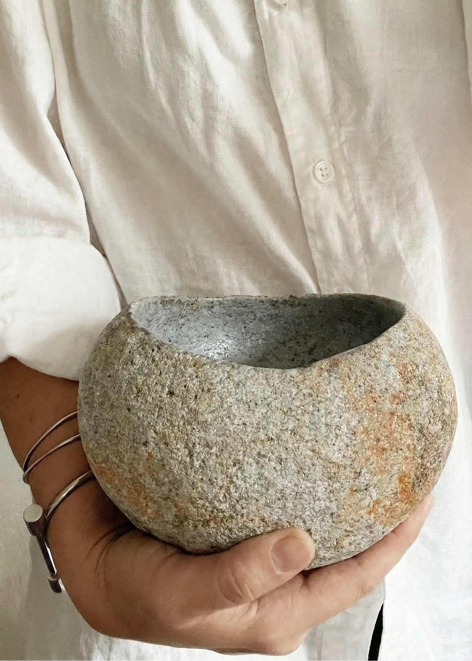 Person holding a textured stone bowl against a white shirt background
