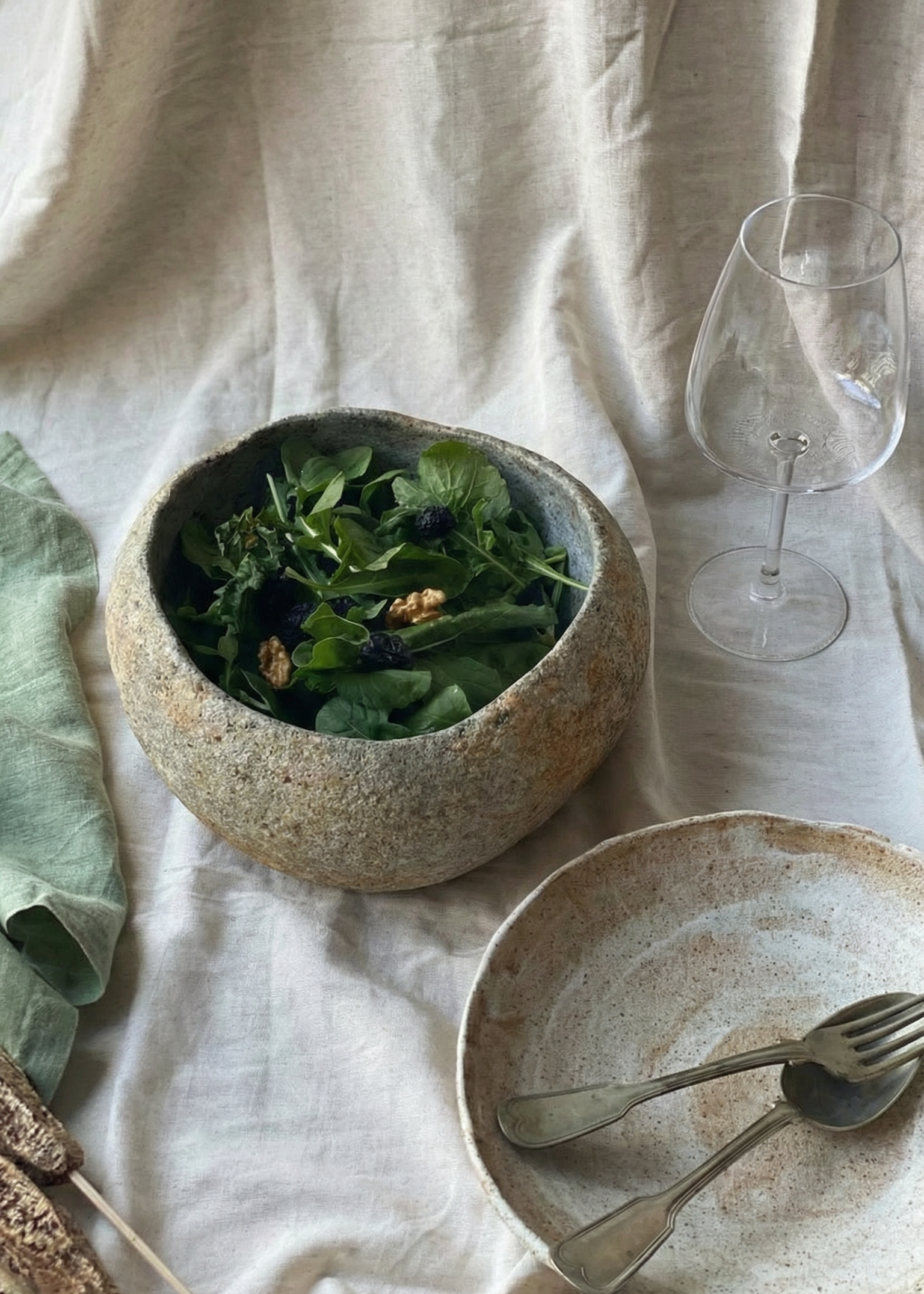 Bowl of salad on a textured surface with a glass and plate.