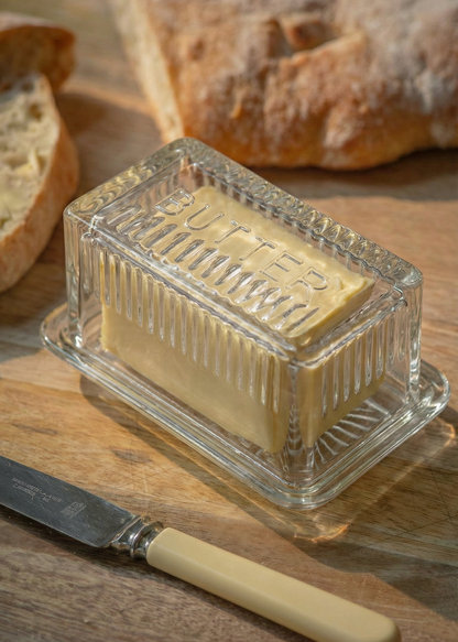 Butter dish with a stick of butter on a wooden board with bread and a knife.