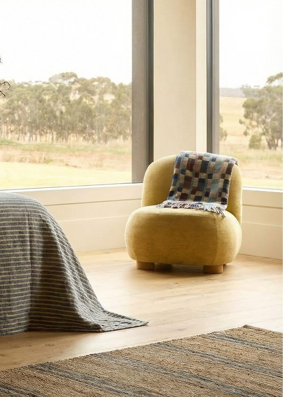 Bedroom with a bed covered in a gray striped blanket, a chair with a patterned throw, and a vase with plants.