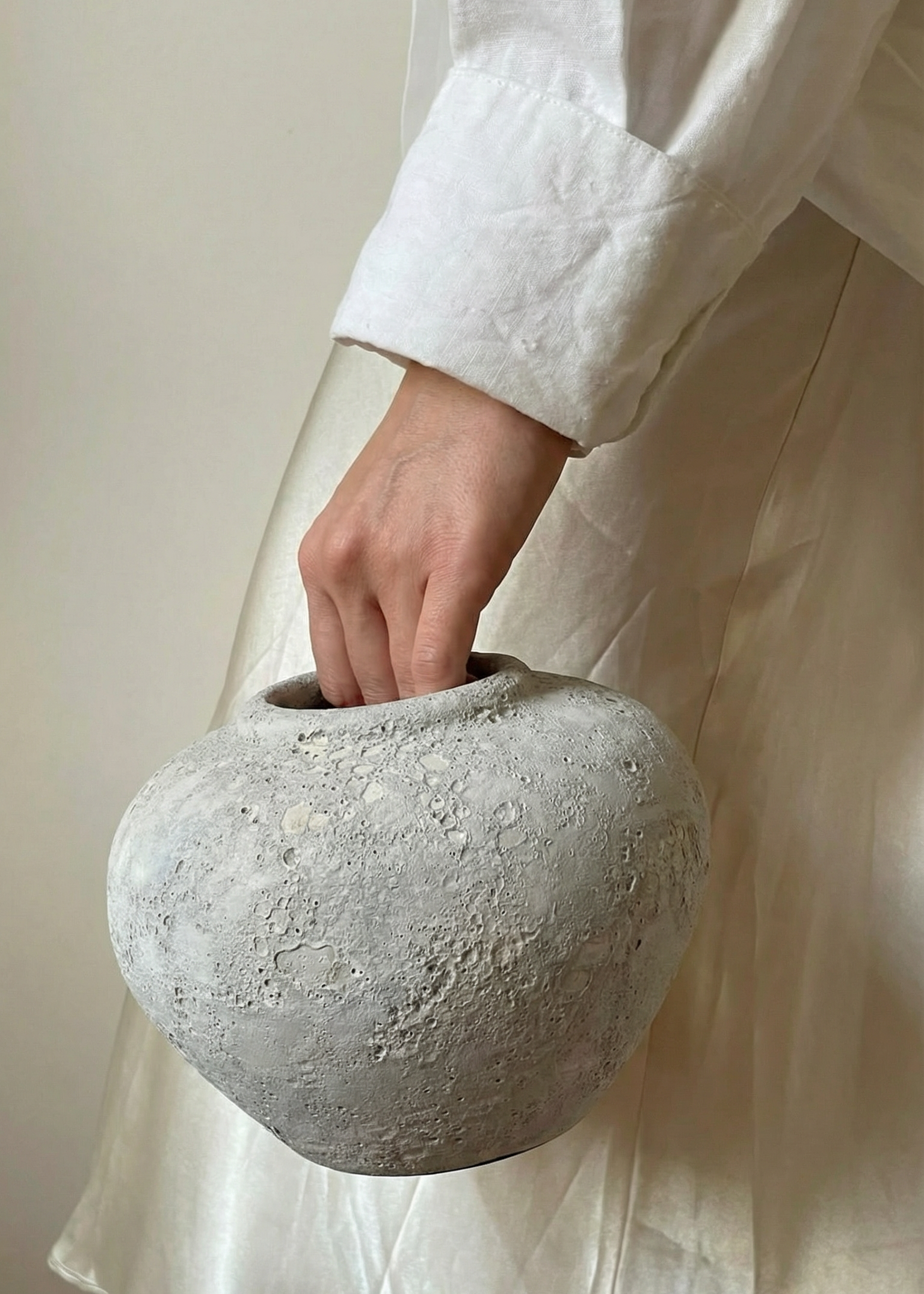 Person holding a textured stone vase against a neutral background