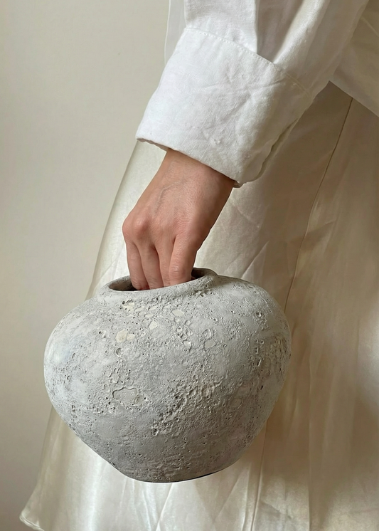 Person holding a textured stone vase against a neutral background