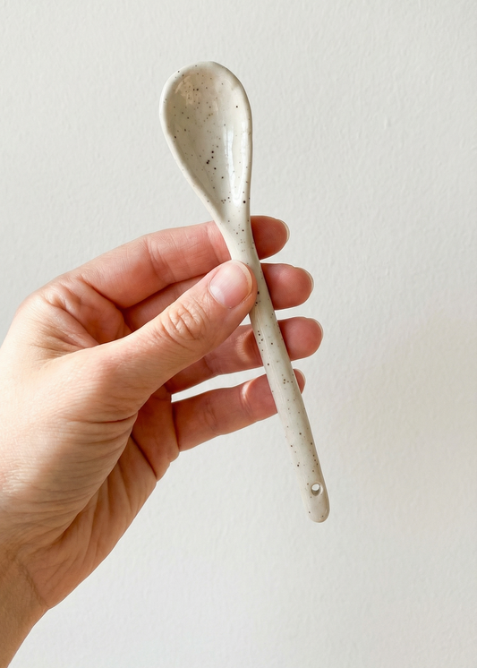 Hand holding a silver spoon against a plain background