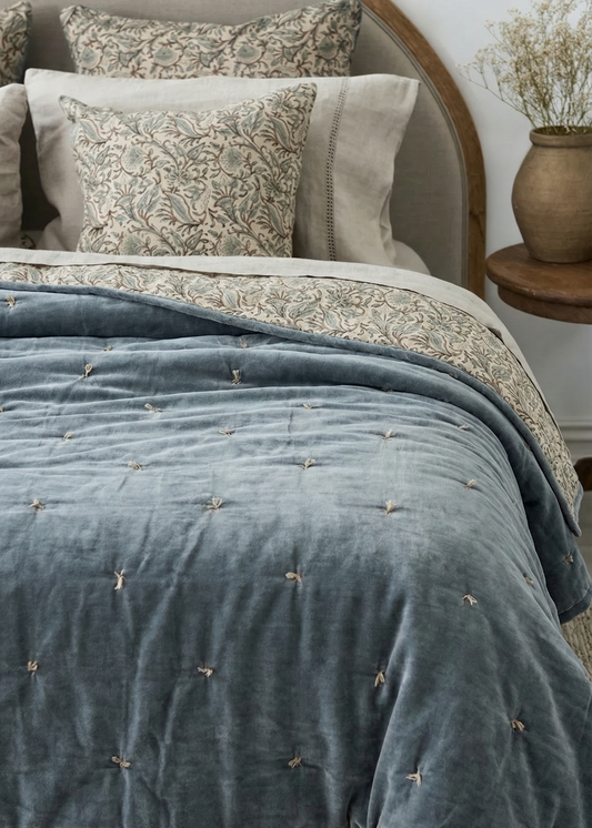Bed with blue textured duvet and floral pillows, wooden headboard and side table.